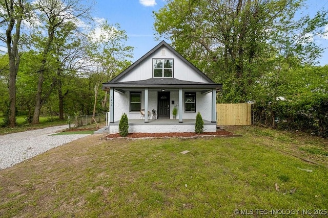 view of front of property featuring a porch, a front yard, fence, and gravel driveway