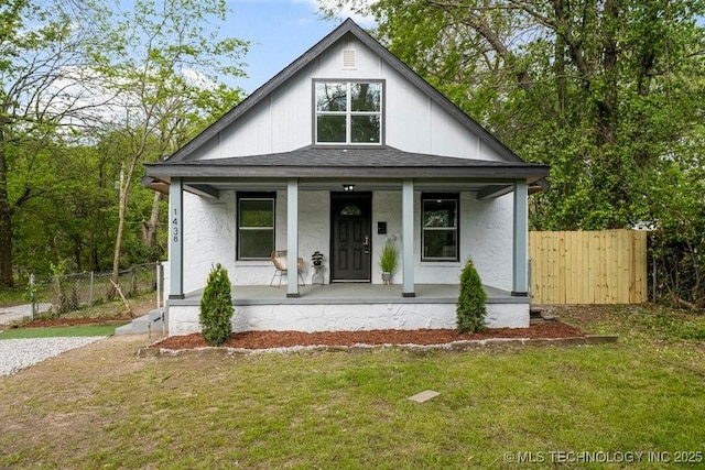 view of front of property featuring covered porch, a front lawn, roof with shingles, and fence