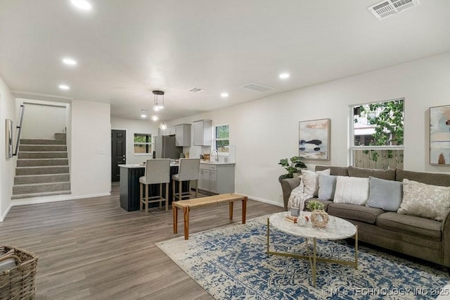 living area with a wealth of natural light, wood finished floors, visible vents, and stairs