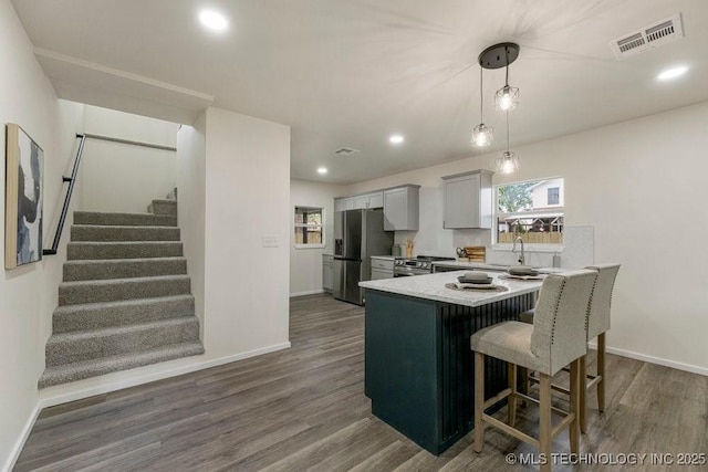 kitchen featuring a breakfast bar area, stainless steel appliances, dark wood-type flooring, visible vents, and light countertops