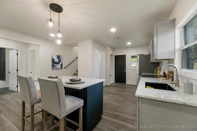 kitchen featuring dark wood-type flooring, a breakfast bar, a kitchen island, a sink, and pendant lighting