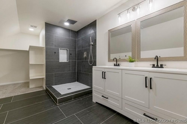 bathroom with double vanity, visible vents, a tile shower, and a sink