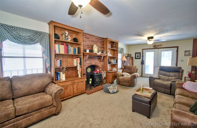 living room with french doors, a ceiling fan, a wood stove, and light colored carpet