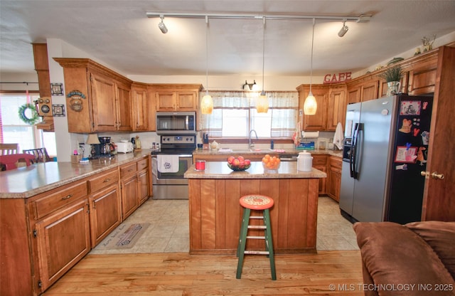 kitchen featuring stainless steel appliances, brown cabinetry, light countertops, and a center island