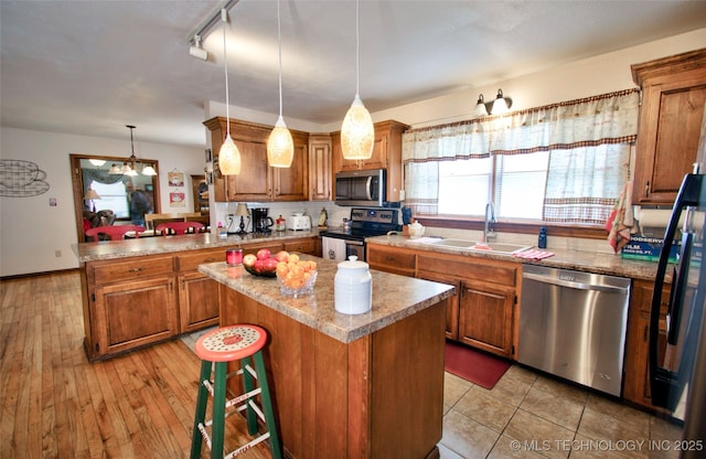 kitchen with appliances with stainless steel finishes, brown cabinetry, a sink, and a center island