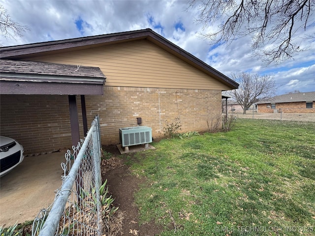 view of home's exterior featuring a yard, brick siding, central AC unit, and fence