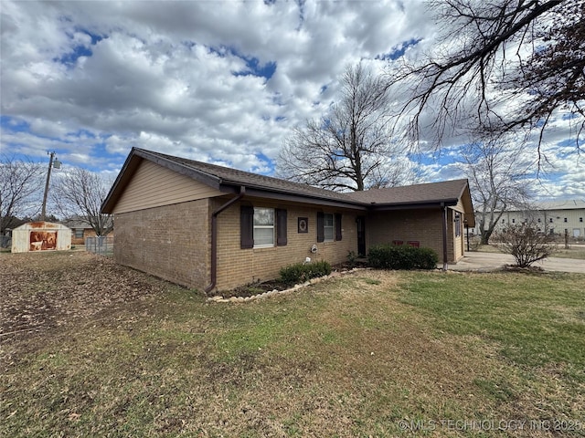 view of side of home featuring an outbuilding, brick siding, a yard, and a storage shed