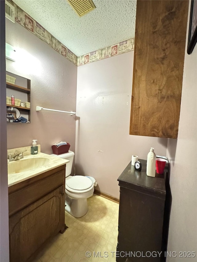 half bath with toilet, vanity, visible vents, baseboards, and tile patterned floors