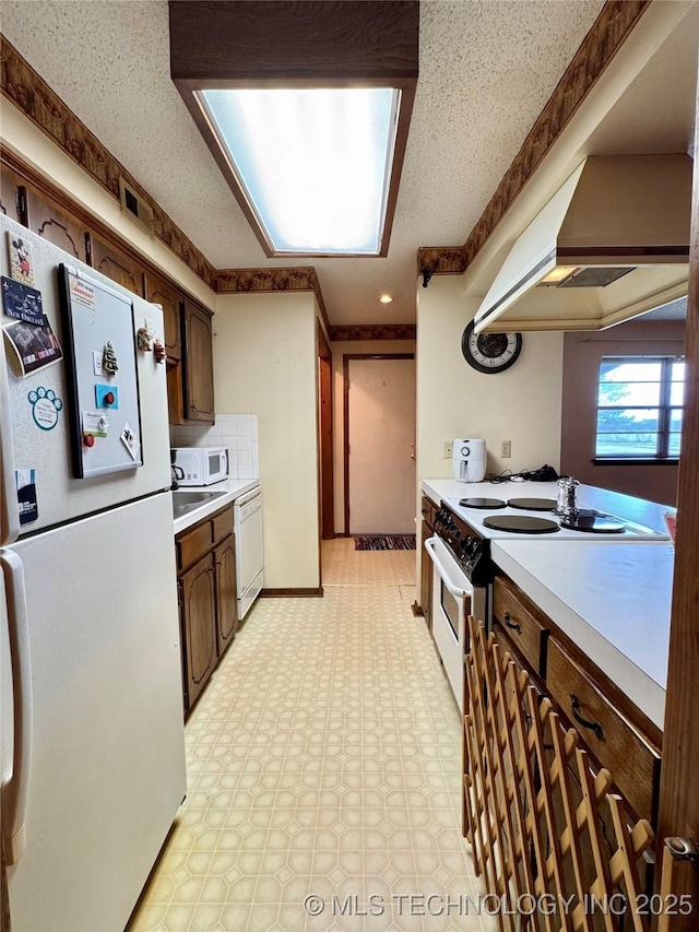 kitchen featuring light countertops, white appliances, light floors, and under cabinet range hood