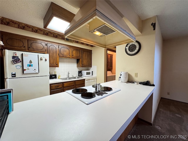 kitchen with washing machine and dryer, a peninsula, white appliances, a sink, and tasteful backsplash