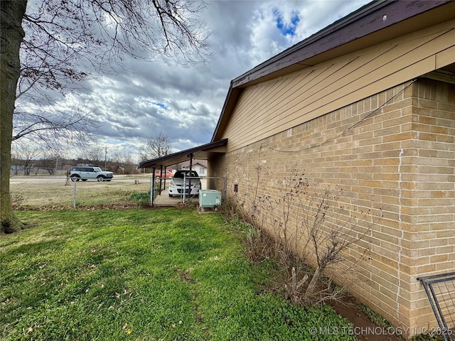 view of side of property featuring brick siding, a lawn, and fence