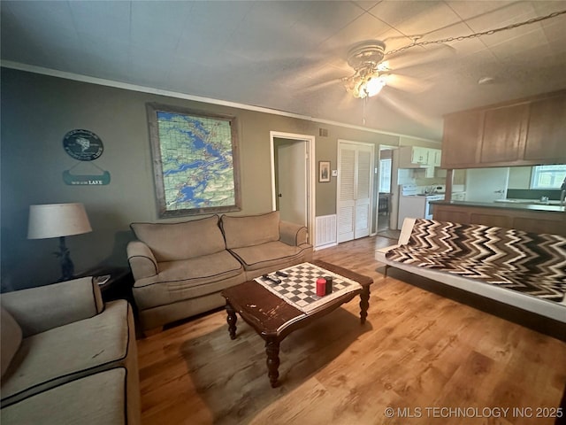 living room featuring crown molding, visible vents, a ceiling fan, and light wood-style floors