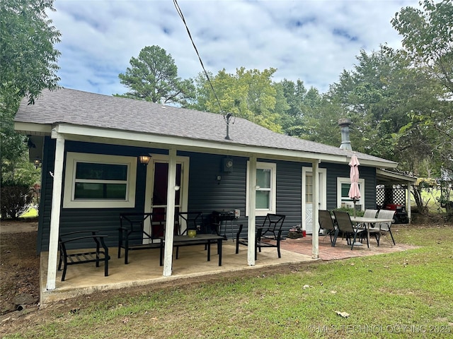 rear view of house with a shingled roof, covered porch, a yard, and a patio