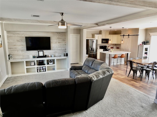 living room featuring a barn door, baseboards, visible vents, a ceiling fan, and light wood-type flooring