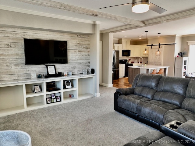 living room with ceiling fan, a barn door, light carpet, an accent wall, and ornamental molding