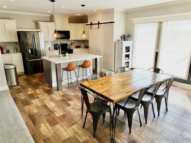 dining area with a barn door, wood finished floors, and crown molding