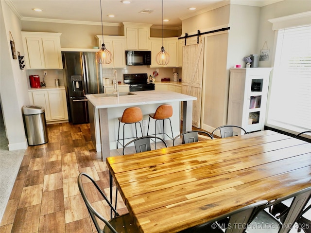 kitchen with a barn door, wood finished floors, light countertops, backsplash, and black appliances