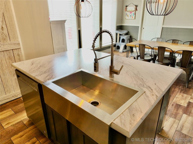 kitchen with light stone counters, a sink, dishwasher, an island with sink, and dark wood finished floors