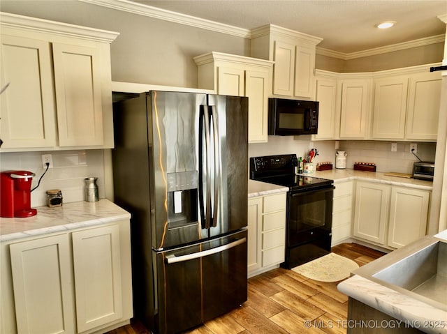 kitchen featuring light wood-style flooring, a sink, backsplash, black appliances, and crown molding