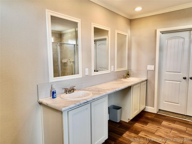 bathroom with double vanity, a stall shower, wood finished floors, crown molding, and a sink