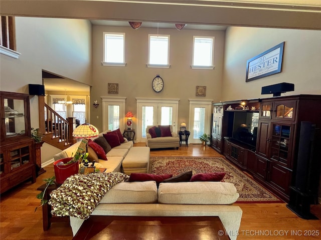 living area with a notable chandelier, stairs, a wealth of natural light, and wood finished floors