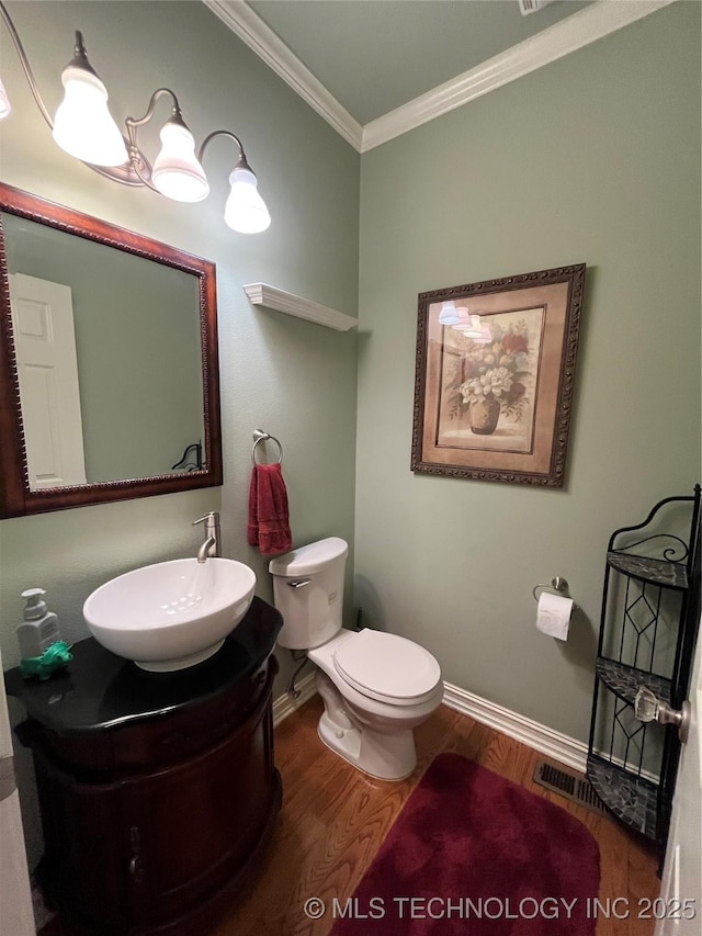 bathroom featuring baseboards, toilet, wood finished floors, crown molding, and vanity