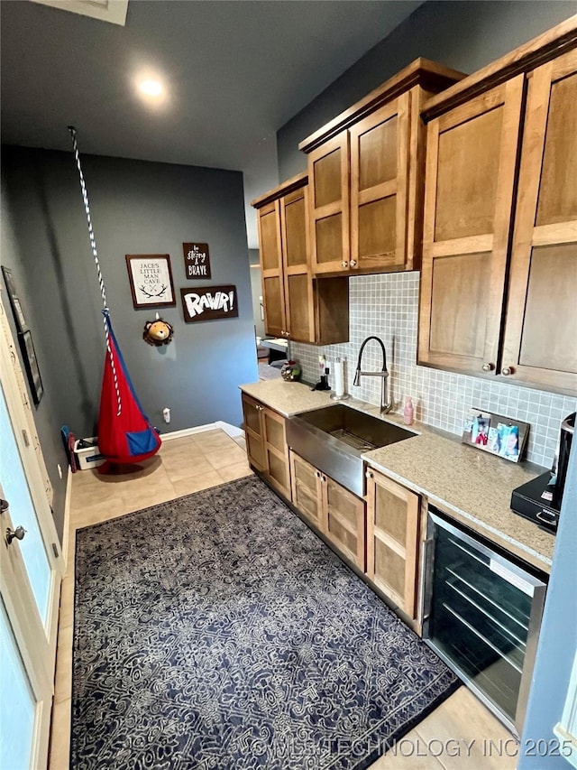 kitchen featuring tasteful backsplash, wine cooler, brown cabinets, light countertops, and a sink