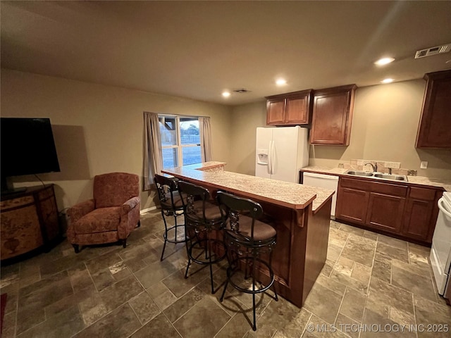 kitchen featuring a breakfast bar, light countertops, visible vents, a sink, and white appliances