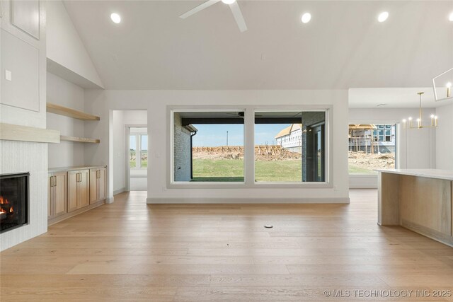2719 E 135th Dr S, Bixby, OK 74008 - unfurnished living room with lofted ceiling, light wood-style flooring, a glass covered fireplace, and a wealth of natural light