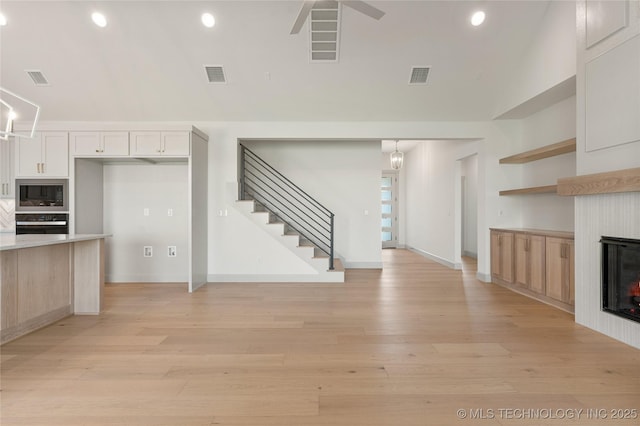 2719 E 135th Dr S, Bixby, OK 74008 - unfurnished living room featuring light wood-type flooring, visible vents, stairs, and a lit fireplace