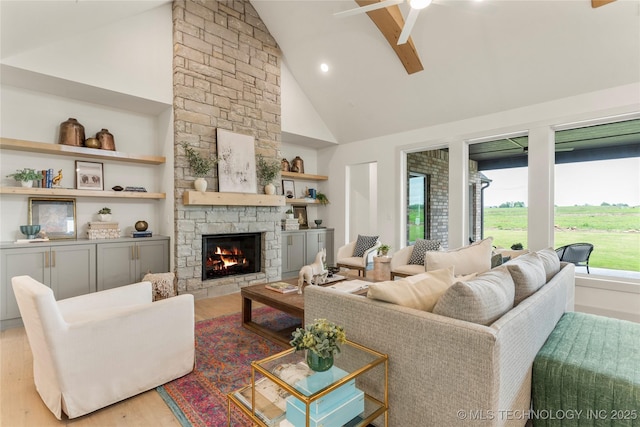 living area with ceiling fan, high vaulted ceiling, a stone fireplace, and wood finished floors