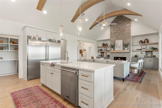 kitchen with white cabinetry, a sink, ceiling fan, stainless steel appliances, and a fireplace