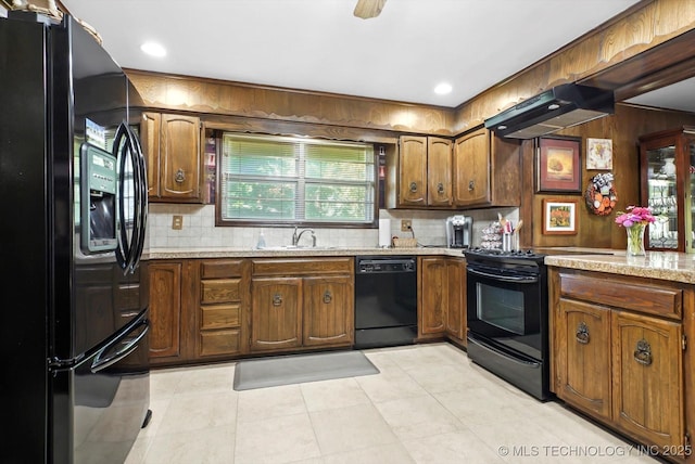 kitchen with decorative backsplash, brown cabinetry, under cabinet range hood, black appliances, and a sink