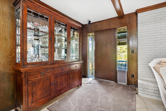 foyer entrance featuring wood walls, beamed ceiling, and light colored carpet