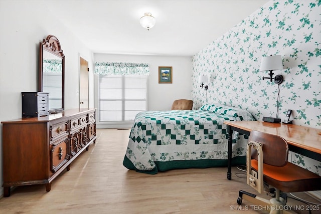 bedroom with an accent wall, light wood-style floors, and wallpapered walls