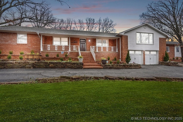 view of front facade with a porch, aphalt driveway, a garage, brick siding, and a yard