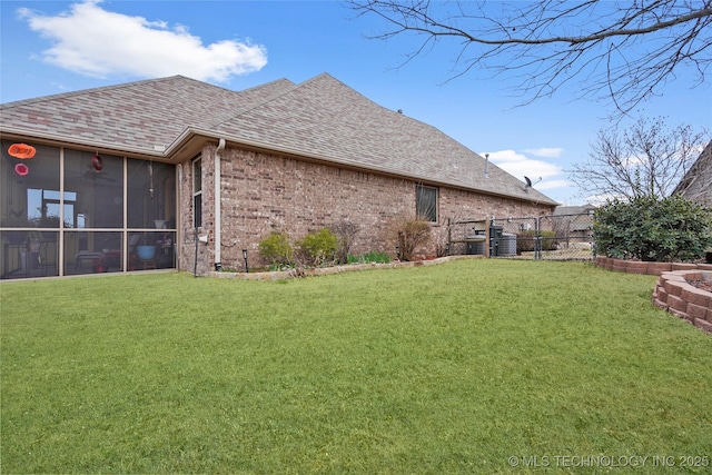 rear view of house with a yard, brick siding, roof with shingles, and a sunroom