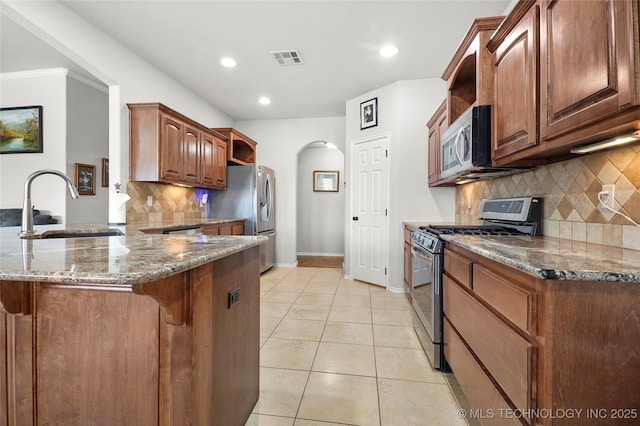 kitchen featuring light tile patterned floors, appliances with stainless steel finishes, a peninsula, arched walkways, and a sink