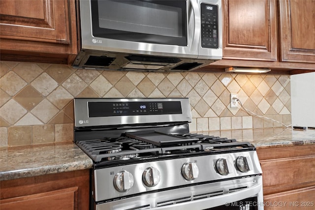 kitchen featuring decorative backsplash, light stone countertops, brown cabinets, and appliances with stainless steel finishes