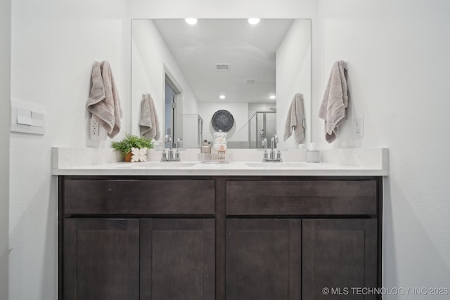 bathroom with double vanity, a shower stall, visible vents, and a sink