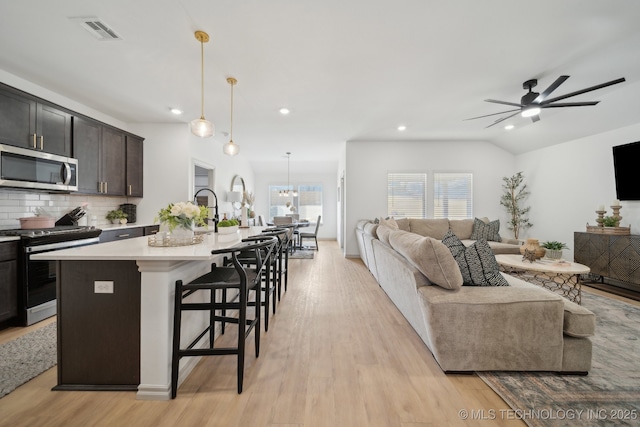 kitchen featuring gas range oven, light countertops, stainless steel microwave, visible vents, and open floor plan