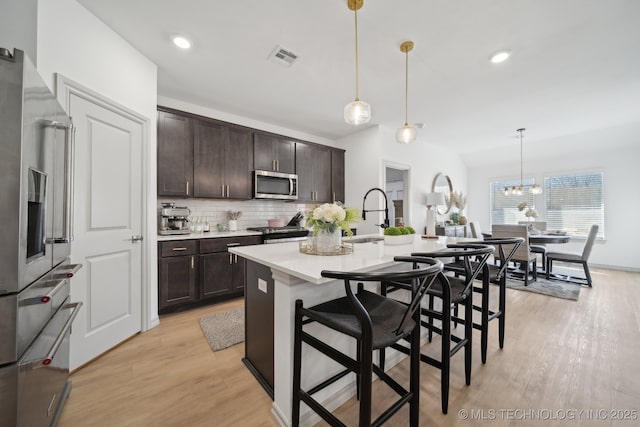 kitchen featuring tasteful backsplash, light countertops, light wood-style flooring, appliances with stainless steel finishes, and dark brown cabinetry