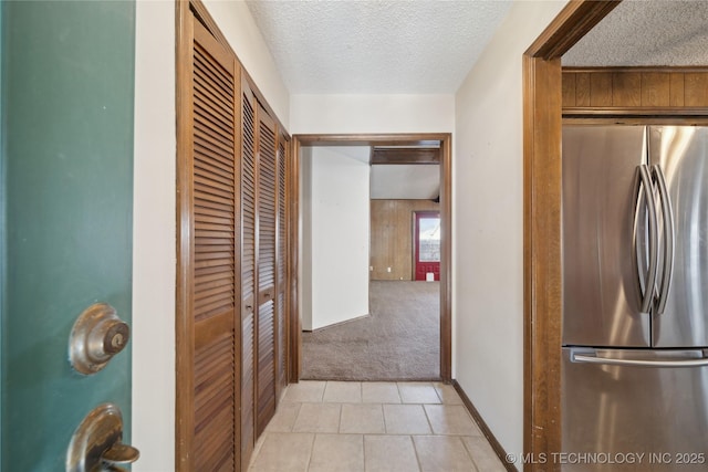 hall featuring baseboards, light colored carpet, wood walls, light tile patterned floors, and a textured ceiling