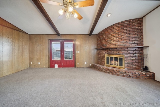 unfurnished living room featuring wood walls, vaulted ceiling with beams, a ceiling fan, and carpet floors