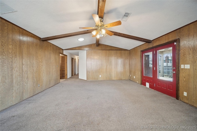 spare room with visible vents, lofted ceiling with beams, wood walls, light colored carpet, and ceiling fan