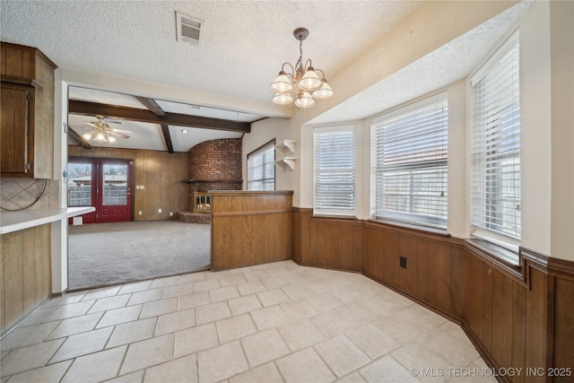 kitchen with visible vents, wooden walls, beamed ceiling, wainscoting, and a textured ceiling