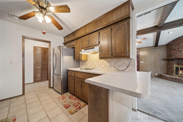 kitchen featuring a peninsula, freestanding refrigerator, ceiling fan, light countertops, and under cabinet range hood