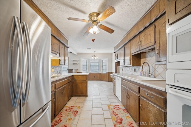 kitchen featuring white appliances, a peninsula, a sink, under cabinet range hood, and brown cabinets