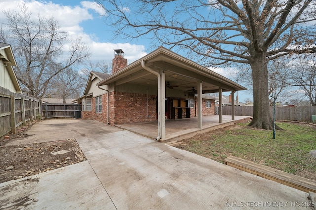 view of property exterior with brick siding, a ceiling fan, a chimney, and fence