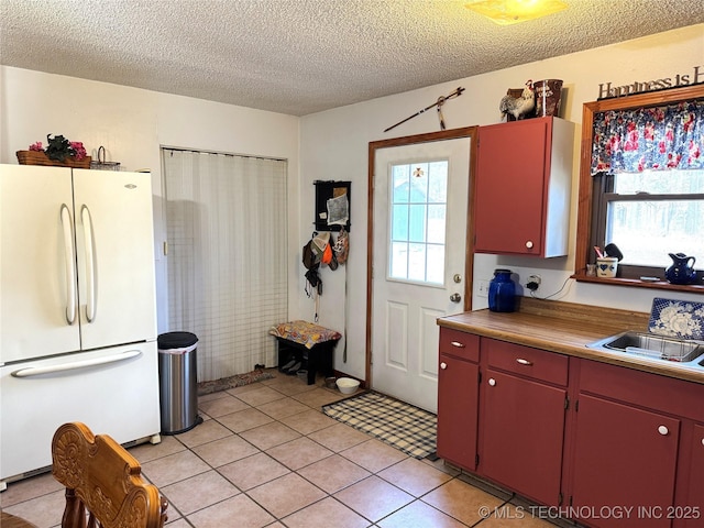 kitchen featuring light tile patterned floors, freestanding refrigerator, red cabinetry, a sink, and a textured ceiling